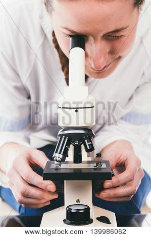 Young woman medical researcher looking through microscope in laboratory