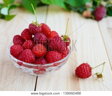 Freshly picked raspberries in a transparent piala on a light wooden background