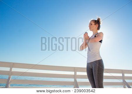Young Slim Woman In Tight Sportswear Practicing Yoga Outdoors At White Wooden Seafront. Girl Standin