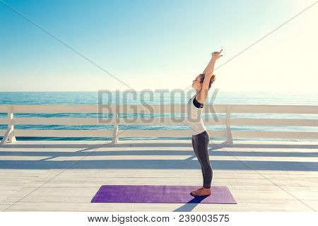 Young Slim Woman In Tight Sportswear Stretching Outdoors At White Wooden Seafront. Girl Standing On 