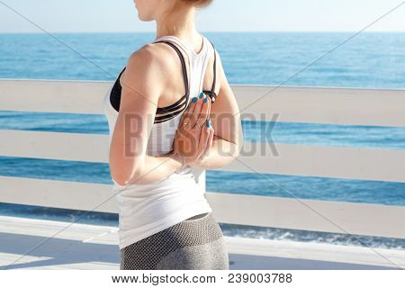 Young Slim Woman In Tight Sportswear Practicing Yoga Outdoors At White Wooden Seafront.