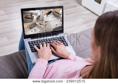 Close-up Of Woman Sitting On Couch Monitoring Home Security Cameras On Laptop At Home