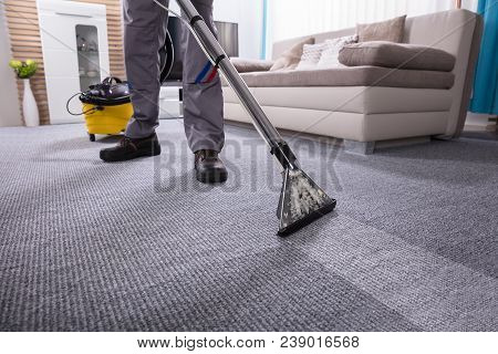 Low Section Of A Person Cleaning The Carpet With Vacuum Cleaner In Living Room