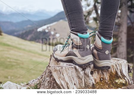 Close up of female classic leather hiking boots wearing by woman standing on stump in mountains - travel and outdoor activities concept
