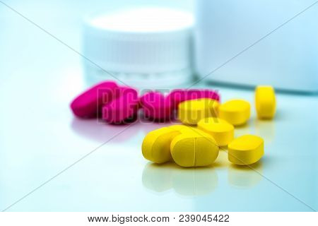 Pile Of Yellow And Pink Tablets Pills On Blurred Background Of Plastic Pills Bottle With Copy Space.