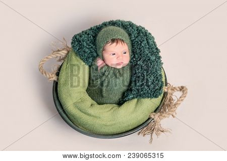 Nwborn swaddled in green coccon lying on basket