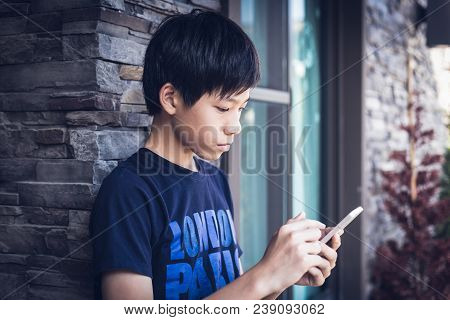Asian Boy Teenager In Dark Blue T-shirt Using Wireless Smartphone For Reading Informantion And Send 