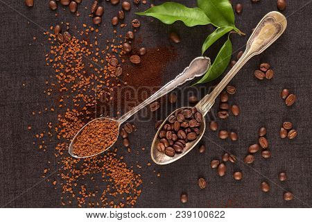 Two Spoons With Roasted Beans And Instant Coffee, Ground And Coffea Leaves On Black Table From Above