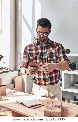 Last Details. Handsome Young Man Putting Greeting Card In The Envelope While Standing Indoors
