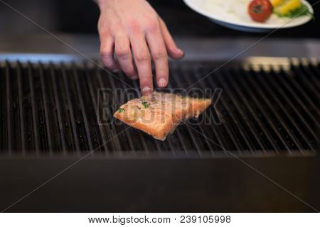 Master chef hands cooking grilled salmon fish with potatoes on a restaurant kitchen