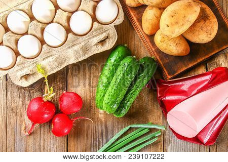 Ingredients For Okroshki - Sausage, Eggs, Radishes, Onions, Potatoes, Cucumbers On An Old Wooden Tab
