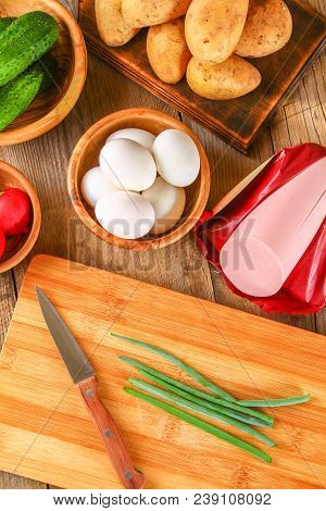 Ingredients For Okroshki - Sausage, Eggs, Radishes, Onions, Potatoes, Cucumbers On An Old Wooden Tab