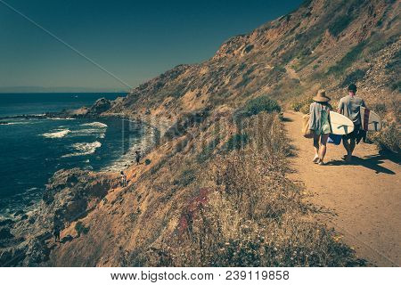 Young Couple Walking On A Rugged Trail With Their Surfboards In Palos Verdes Estates, California
