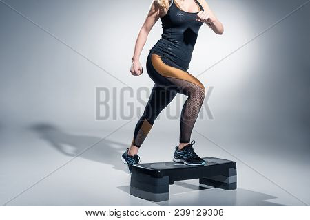 Young Woman Exercising On Step Platform On Grey Background