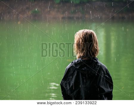 Young Person Sitting On A Bank In The Rain Looking On A Lake
