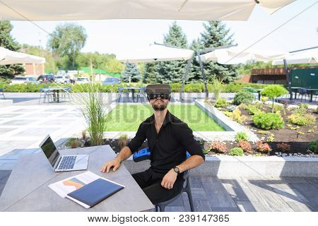 Male Businessperson Enjoying With Virtual Reality Glasses, Working With Laptop And Papers Under Beac