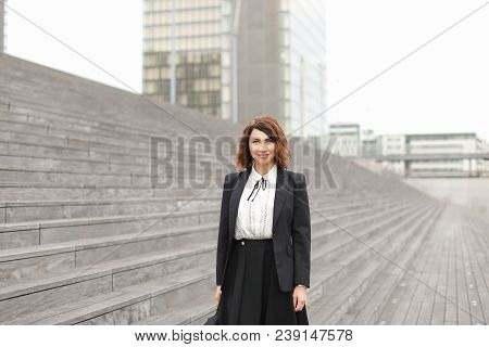 American Secretary Standing On Stairs With Bag And High Buildings In Background. Concept Of Professi