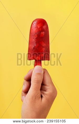 closeup of a young caucasian man with a homemade natural ice pop in his hand, against a yellow background