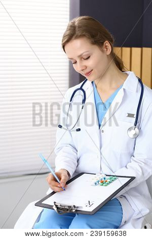 Woman Doctor Write Prescription While Sitting In Hospital Office. A Lot Of Various Colored Pills Liy