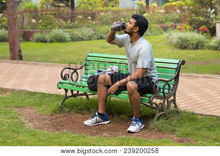 Young Athlete Drinking Water While Resting In Park Bench