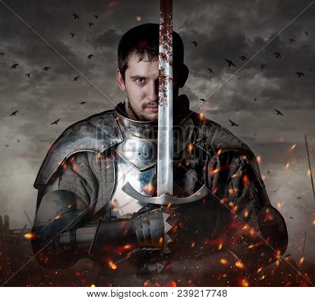 Knight With Sword In Battlefield With Dark Clouds On Background.