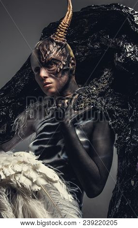 Portrait Of Devil Woman In Black And White Clothes With One Horn On Her Head. Isolated On Grey Backg