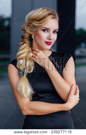 Attractive Lady With Blong Hair In Long Evening Dress Stands Next To The Building With Mirror Window