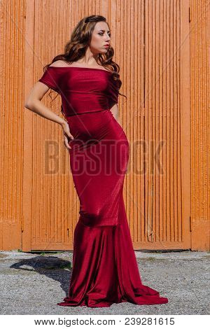 Beautiful Young Woman In A Long Red Evening Gown With A Train Standing Next To The Old Door