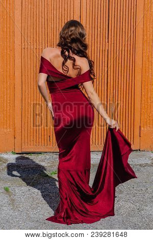 Back View Of A Beautiful Young Woman In A Long Red Evening Gown With A Train Standing Next To The Ol