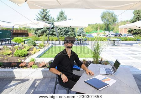 American Businessman Enjoying With Virtual Reality Glasses, Working With Laptop And Papers Under Bea