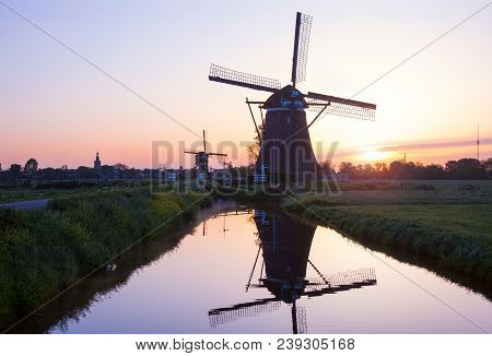 Traditional Dutch Windmills Reflected In The Calm Water Of The Canal.  Landscape With Old Windmills 