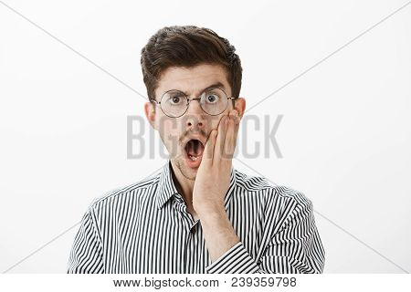 Indoor Shot Of Shocked Emotive Adult Male Coworker In Glasses, Dropping Jaw And Holding Palm On Chee