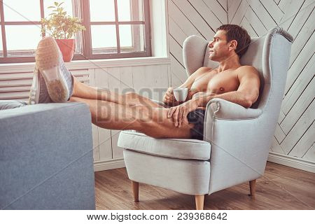 Handsome Shirtless Muscular Man Lying On The Chair, Drink Cup Of Tea, Resting After A Hard Workout A