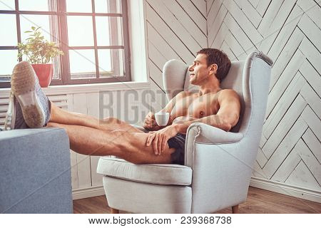 Handsome Shirtless Muscular Man Lying On The Chair, Drink Cup Of Tea, Resting After A Hard Workout A