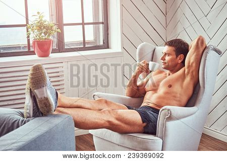 Handsome Shirtless Muscular Man Lying On The Chair, Drink Cup Of Tea, Resting After A Hard Workout A