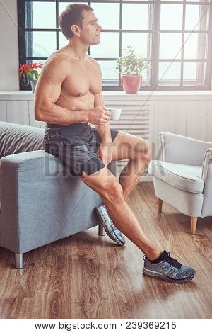 Handsome Shirtless Muscular Male Lying On The Sofa, Drink Cup Of Tea, Resting After A Hard Workout A