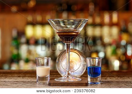 A Cocktail Based On Sambuca And Liqueurs Stands On A Wooden Counter In A Night Club Or In A Pub. The