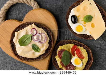 Open  faced  sandwich canape or crostini on a wooden serving board on dark stone background closeup. Top view.