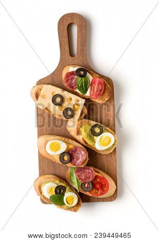Open faced sandwich canape or crostini on a wooden serving board isolated on white background closeup. Top view.