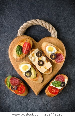 Open faced sandwich canape or crostini on a wooden serving board on dark stone  background closeup. Top view.