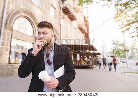 A Business Man With Documents In His Hands Eats A Snack While Walking To Work. A Busy Man Bites A Sa