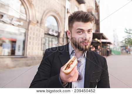 Happy Business Man Stands In The Street With A Sandwich In His Hands And Looks At The Camera. Fast F