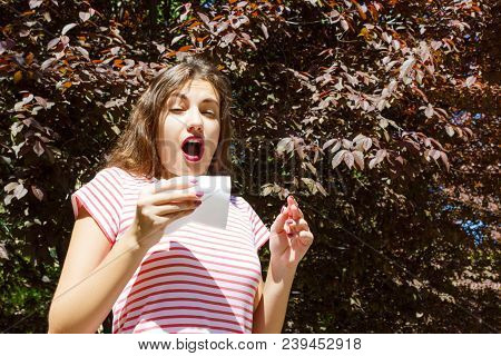 Allergy Concept. Sneezing Young Girl With Nose Wiper Among Blooming Trees In Park