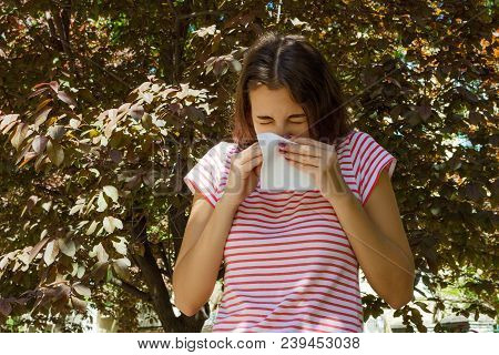 Allergy Concept. Sneezing Young Girl With Nose Wiper Among Blooming Trees In Park