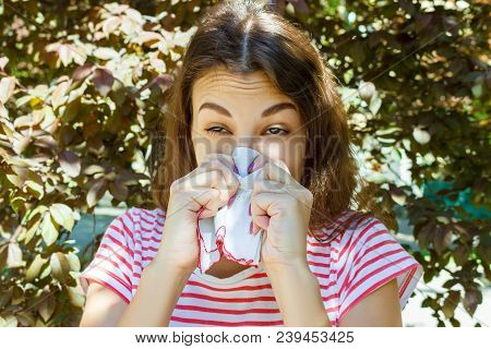Young Girl With Allergy In Autumn Park. Sneezing Girl Blows Her Nose In A Napkin