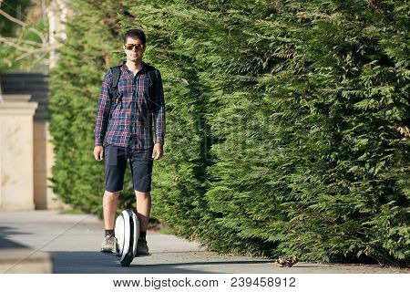 A Stylish Guy Moves Along The Sidewalk On A Mono-wheel.