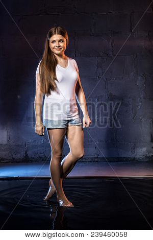Girl In White Shirt Stands In Small Pool During Photoshoot With Water And Black Wall Illuminated Col