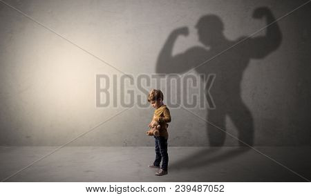 Little waggish boy in an empty room with musclemen shadow behind