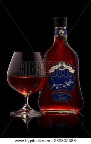 Bottle of cognac Jacques Laffitte XO Superior  and glass with cognac on a black background with reflection.