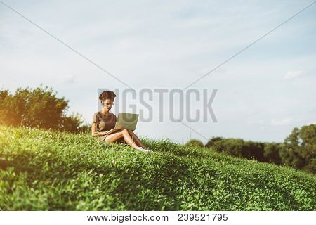 A Pensive Young African-american Woman Is Sitting Alone On The Grass Of The Flank Of The Hill And Us